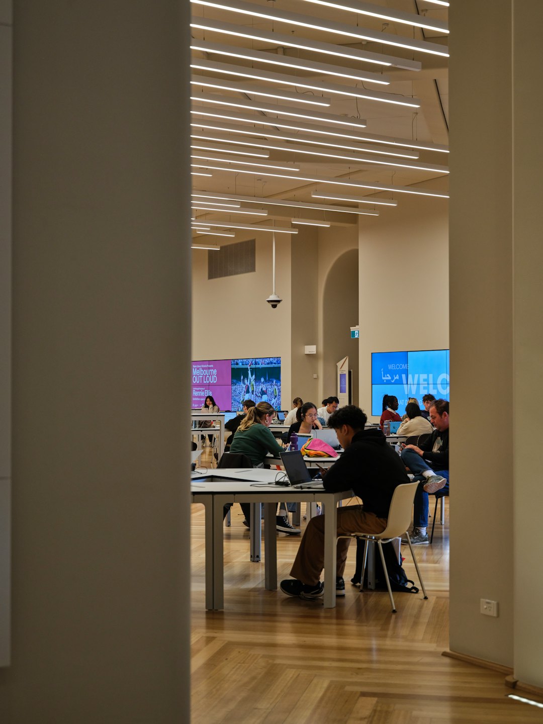 Students sit at tables working on laptops in a library.