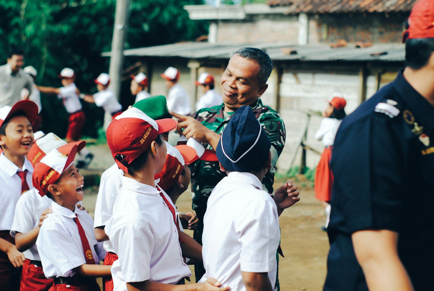 A soldier in camouflage uniform laughing with a group of school children.