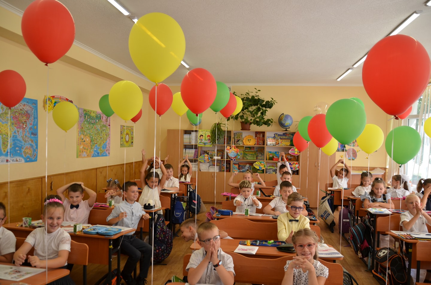 Students sit at desks in a classroom filled with balloons.