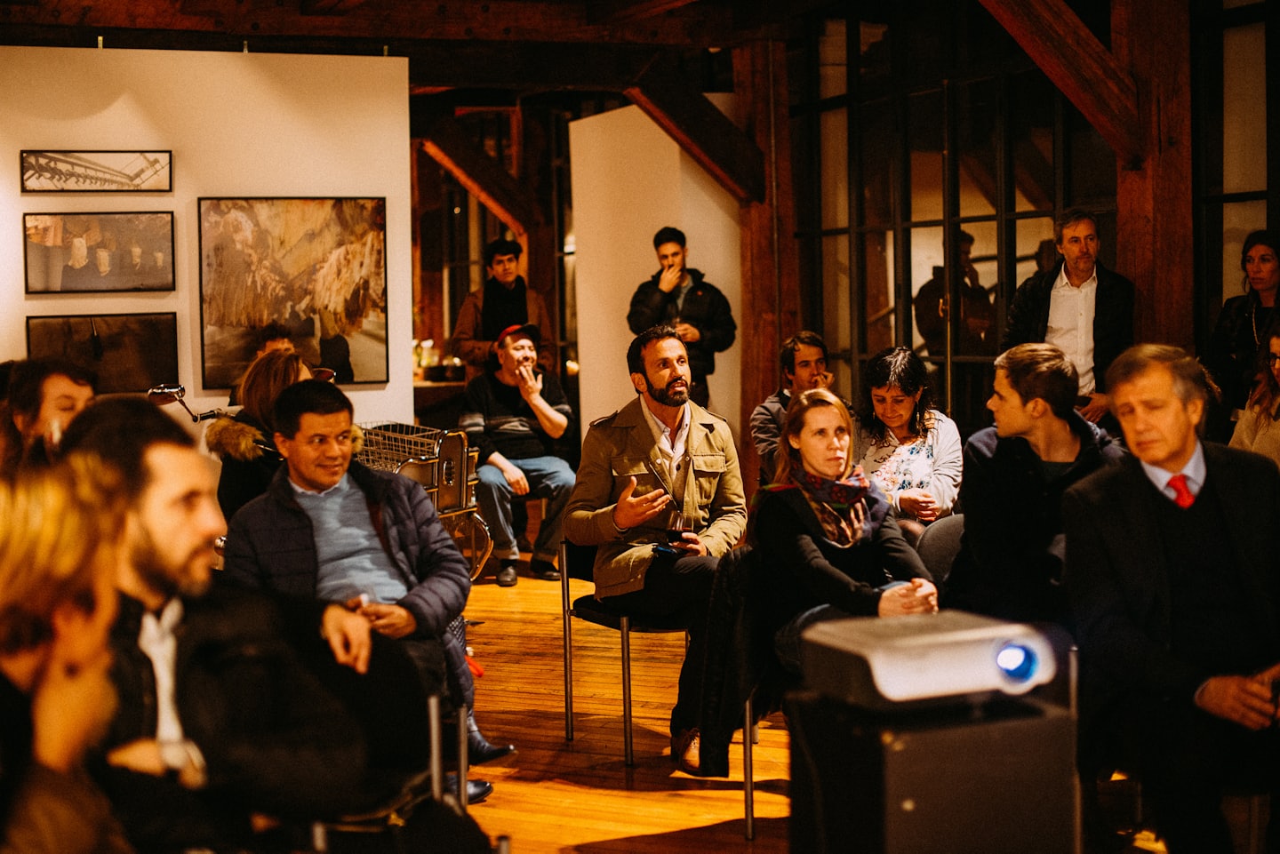 Adults listen attentively at an indoor event with a projector.