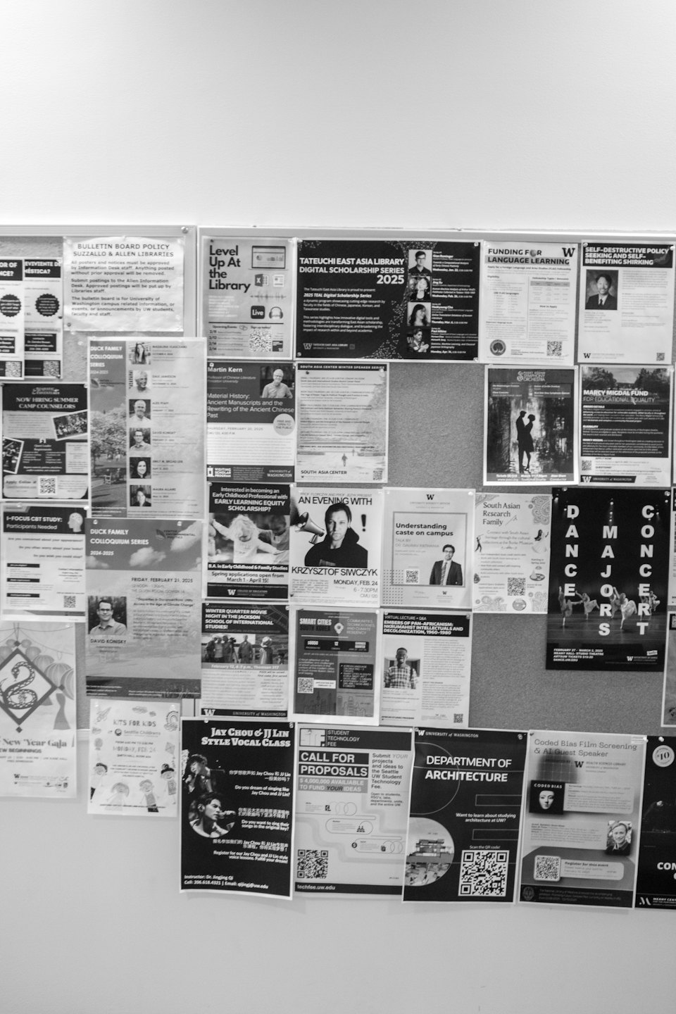 Bulletin board covered with many overlapping posters and flyers.